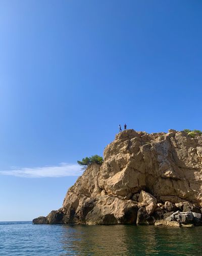 Rock formations by sea against clear blue sky