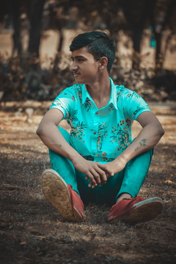 Young man looking away while sitting on land