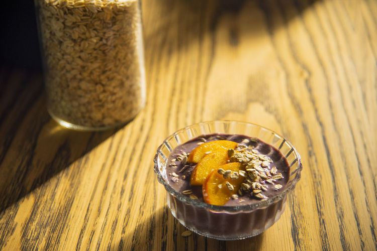 Acai smoothie, granola, seeds, fresh fruits in a glass bowl on wooden table. eating  breakfast bowl