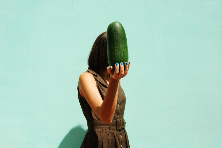 View of woman holding vegetable against wall
