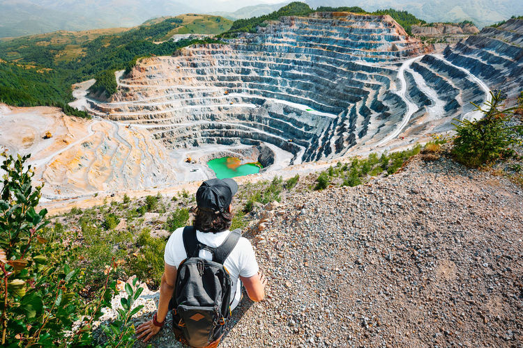Rear view of man with backpack looking at gold and copper quarry mine