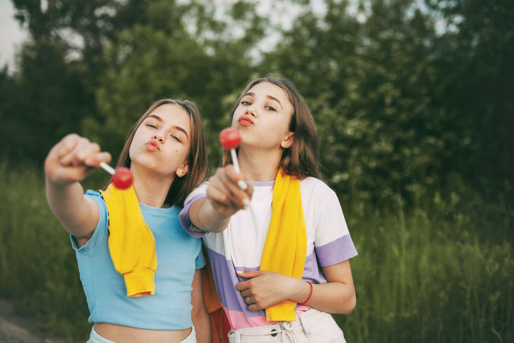 Portrait of friends holding lollipops standing against plants in park