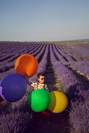 Fashionable baby boy in colorful clothes with dot holds balloon in blooming lavender field in summer