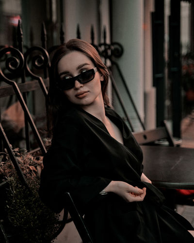 Portrait of young woman wearing sunglasses while standing in cafe
