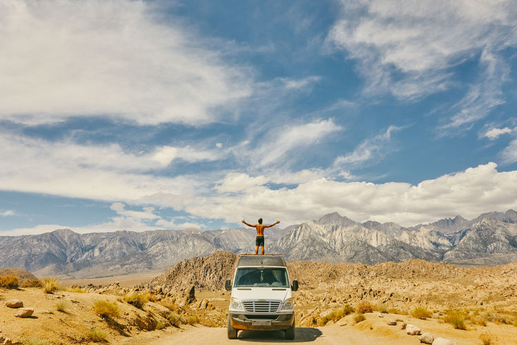 Young man on roof of camper van with open arms in northern california.