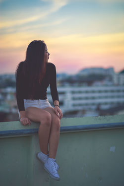 Woman sitting on railing during sunset