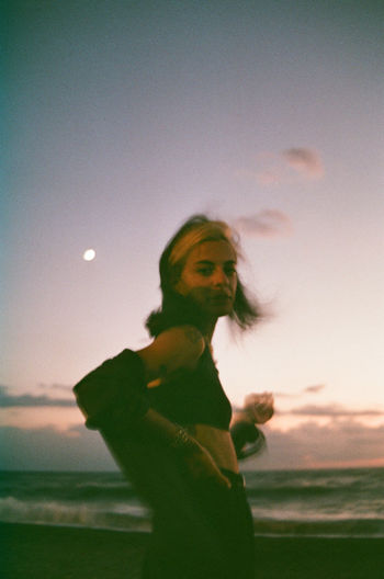Woman by sea against sky during sunset