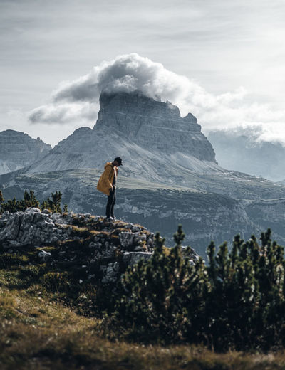 Man standing on rock by mountain against sky