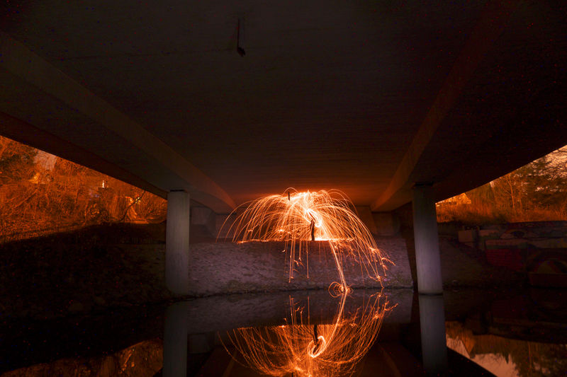 Person spinning wire wool under bridge at nigh