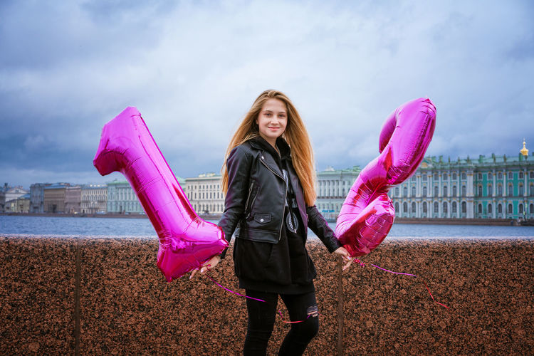 Happy girl holding balloons on the embankment of the city in a leather jacket.