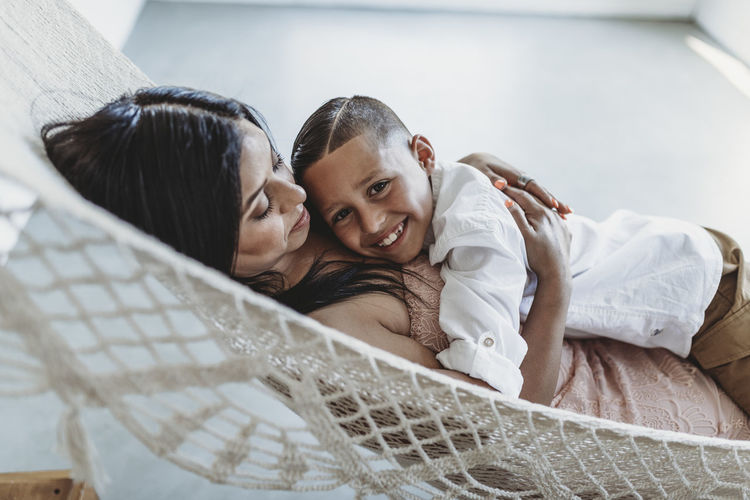 Mother and young son cuddling while laying in hammock in studio