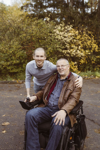 Portrait of smiling young man with arm around father in motorized wheelchair