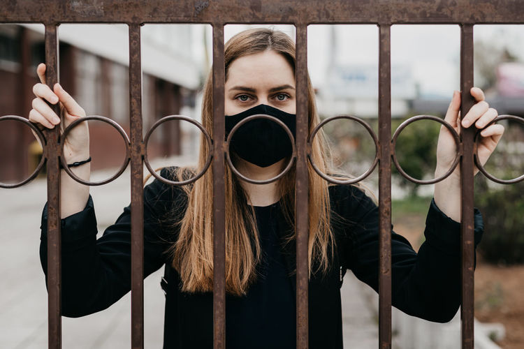 Woman with face mask behind the bars outdoors, concept lockdown covid 19