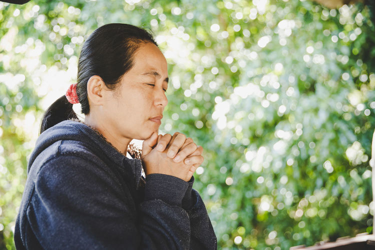 Woman praying in nature, the girl thanks god with her hands folded at her chin,.
