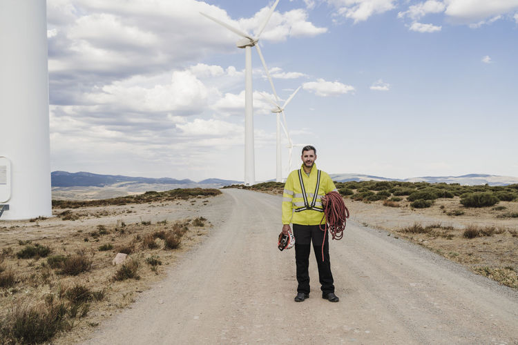 Engineer with helmet and rope standing on road at wind farm