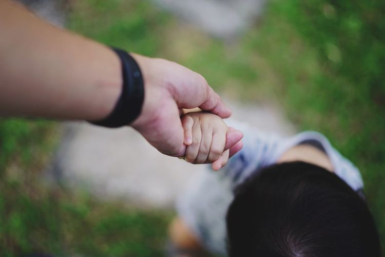 Cropped image of mother holding son hand on field