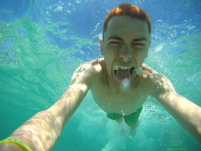 Shirtless man making face while swimming underwater in pool