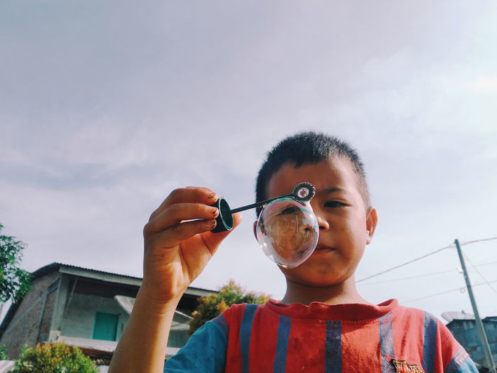 Low angle view of boy looking at bubble against sky