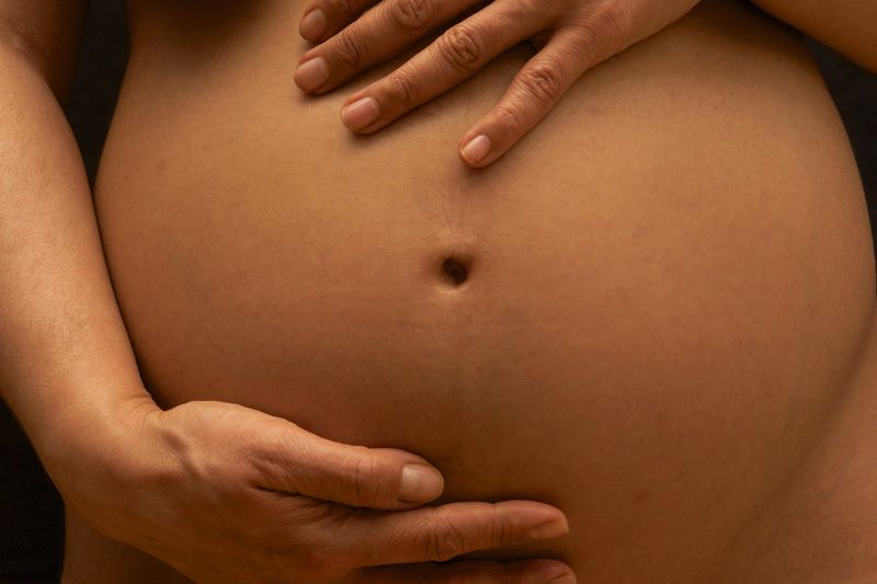 Close-up of pregnant woman holding belly against black background