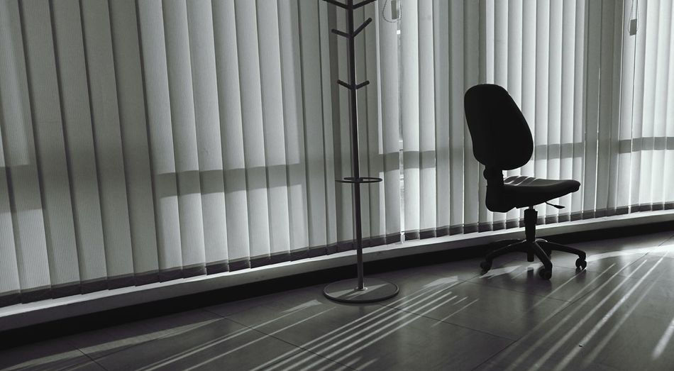 Empty chair by window blinds in office