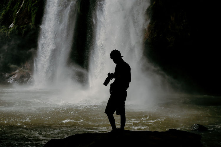 Silhouette man standing against waterfall