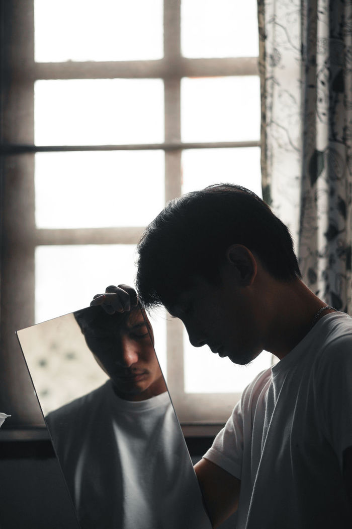 Man holding mirror against window at home