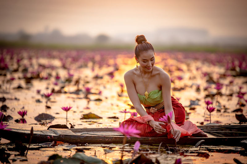 Woman holding lotus while sitting on boat in lake