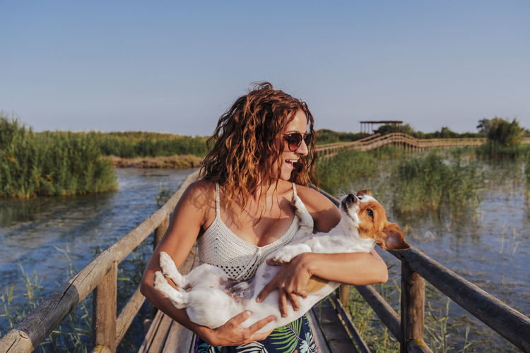 Smiling woman with dog on footbridge against sky