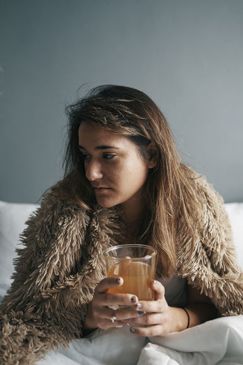 Close-up of woman holding lemon tea sitting on bed