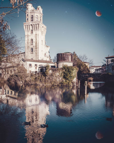 Reflection of buildings and trees in river against sky