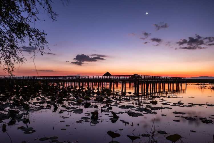 Silhouette wooden posts on beach against sky during sunset