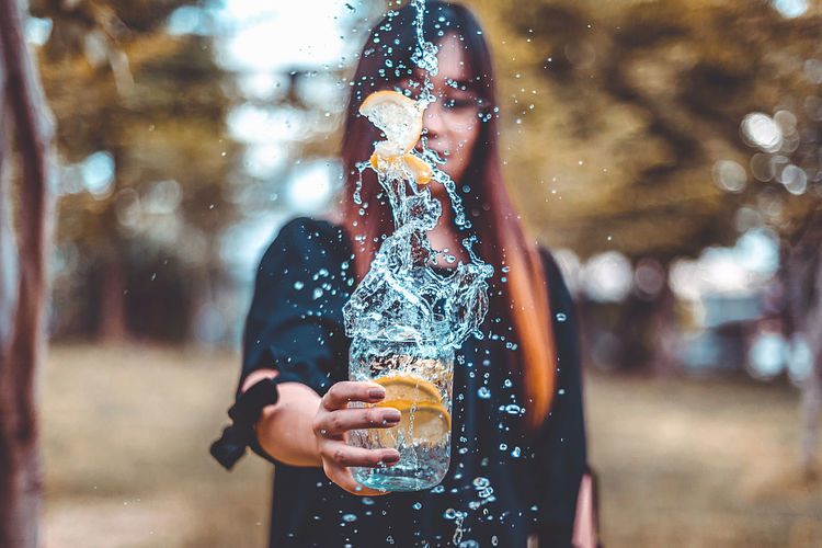 Woman holding lemon slices falling in drink while standing outdoors