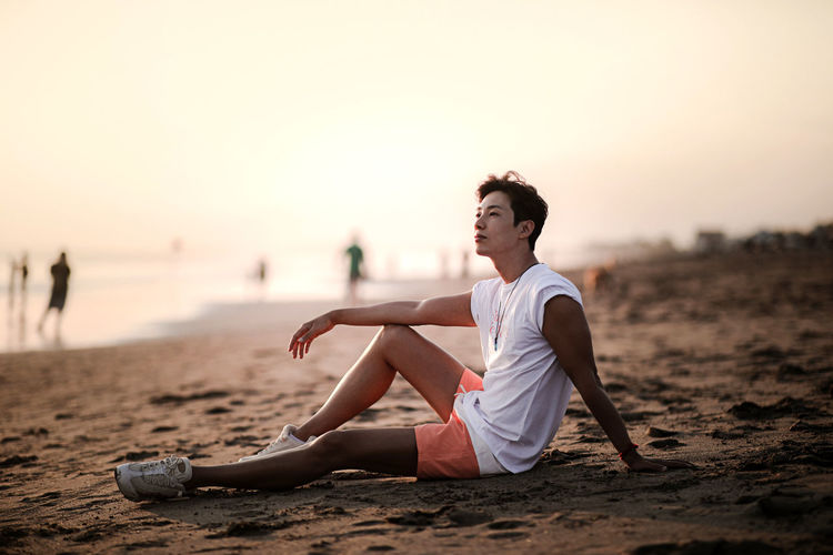 Full length of man sitting on sand at beach against sky