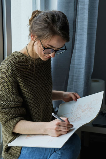 Millennial girl draws fabulous images on paper while sitting at home
