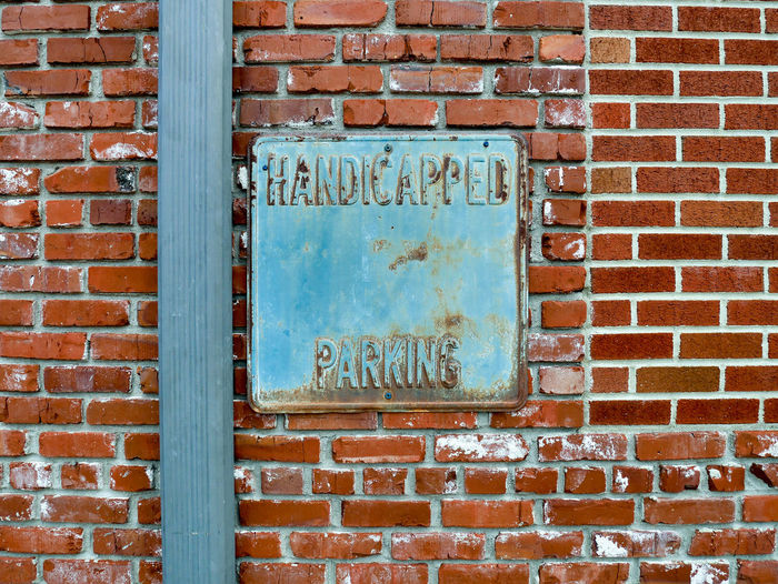 Old metal handicapped parking sign on brick wall