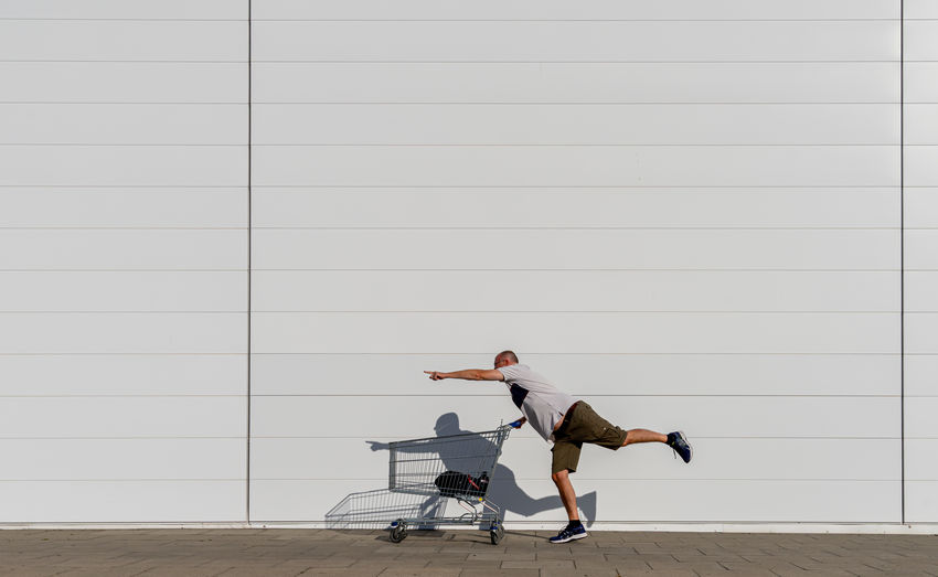Side view of man with shopping cart standing against wall