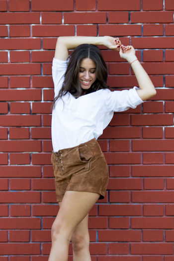 Full length of smiling young woman standing against brick wall