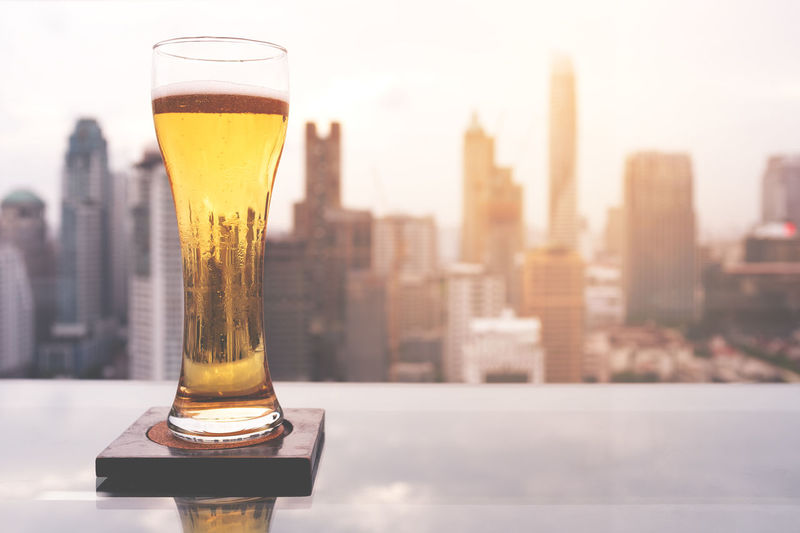 Close-up of beer glass on table against cityscape