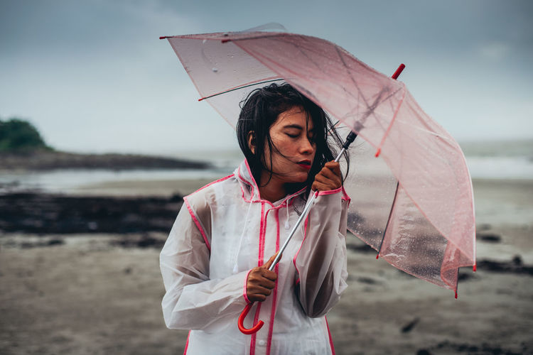 Woman holding umbrella while standing at beach
