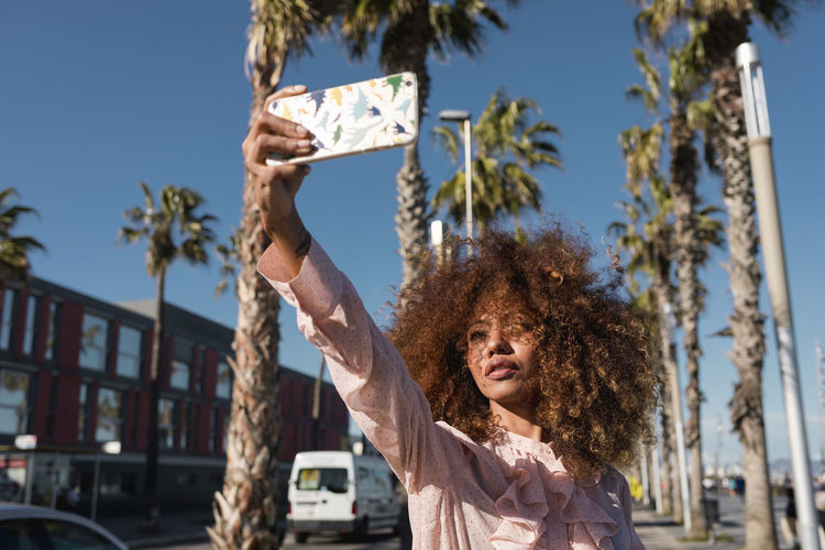 Stylish young woman taking a selfie at seaside promenade