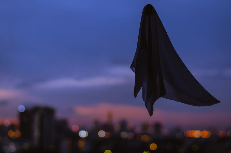 Ghost sheet flying in dusk sky with city lights background. halloween scary concept.