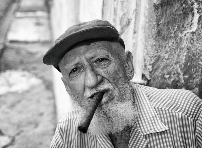 Portrait of senior man wearing cap smoking cigar