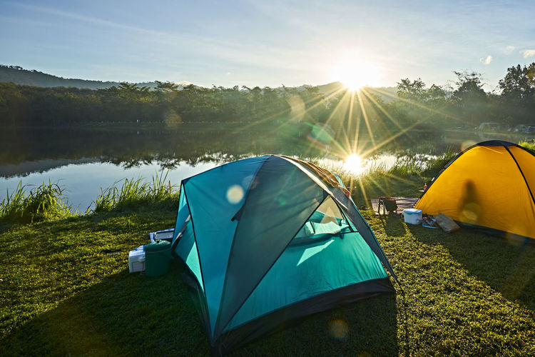 Tents on field by lake against bright sun