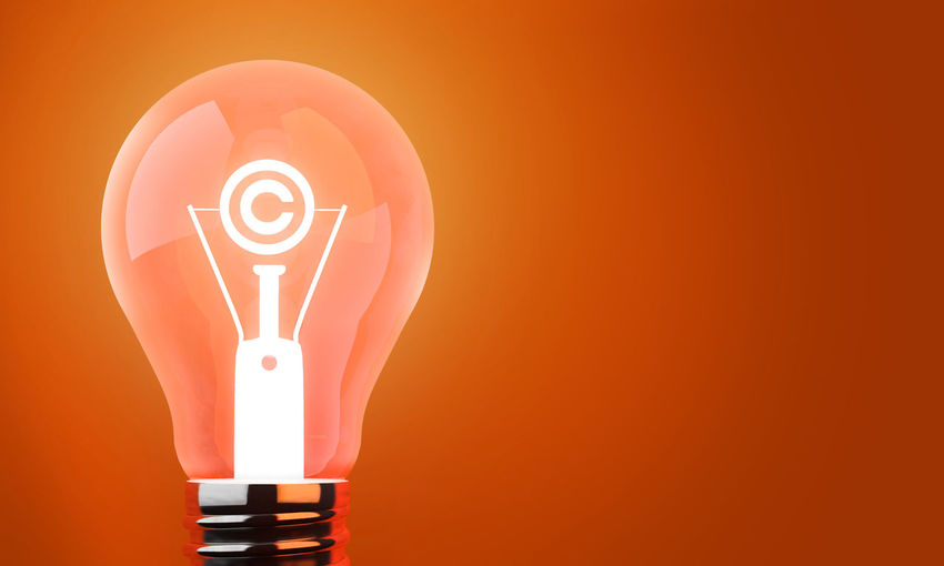 Digitally generated image of illuminated light bulb against orange background