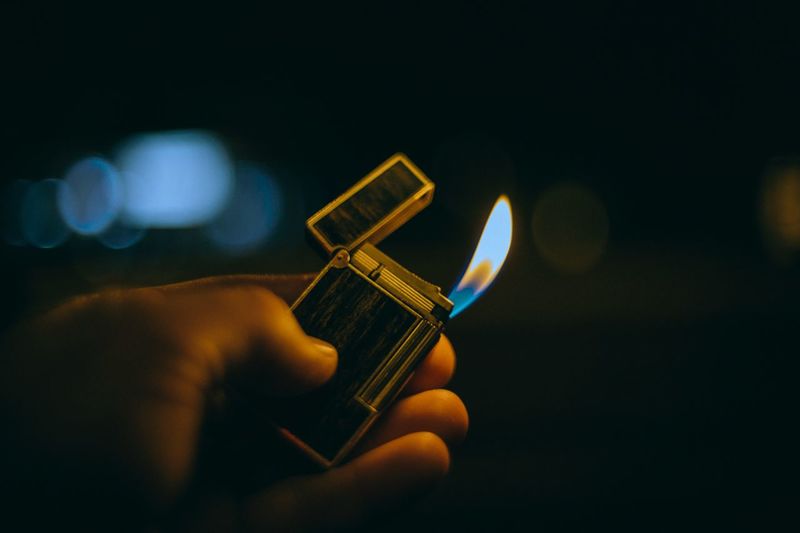 Cropped hand holding lit cigarette lighter at night