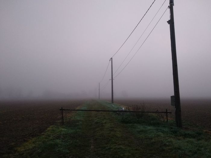 Electricity pylon on field against sky during foggy weather