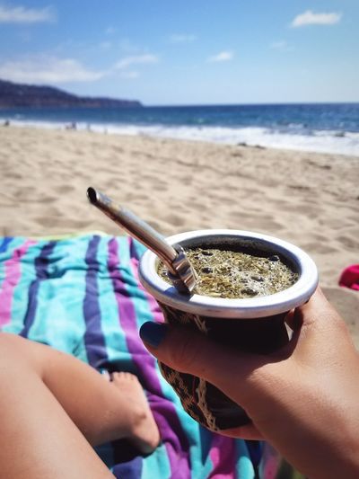 Close-up of hand holding coffee cup on beach