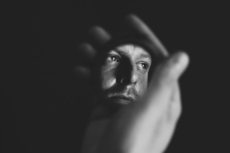 Cropped hand holding mirror with reflection of man against black background