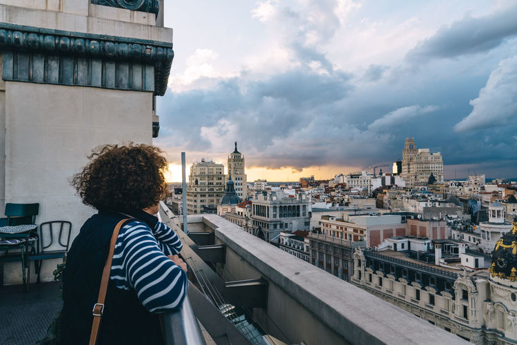 Side view of woman looking at city against cloudy sky
