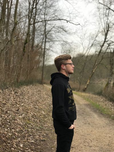 Side view of young man looking away while standing against bare trees